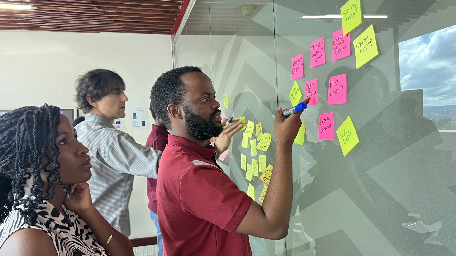 EAB fellows and faculty clustering sticky notes on a glass wall during a brainstorming session