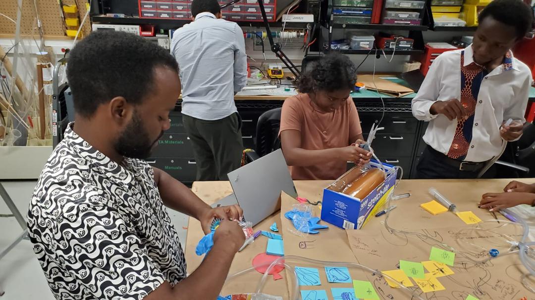 EAB fellows building an early prototype from tubing and sketch cards at a lab workbench