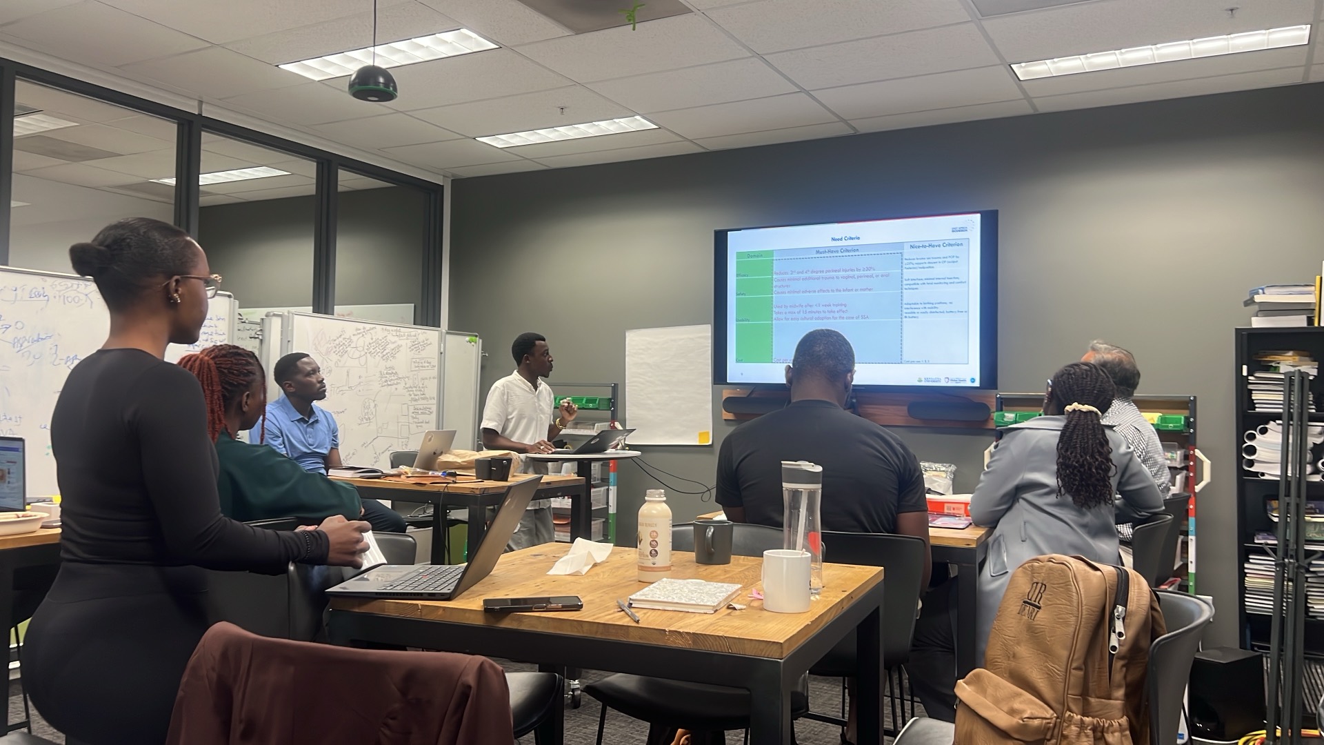 An EAB fellow presenting need criteria to the cohort on a large screen during a working session