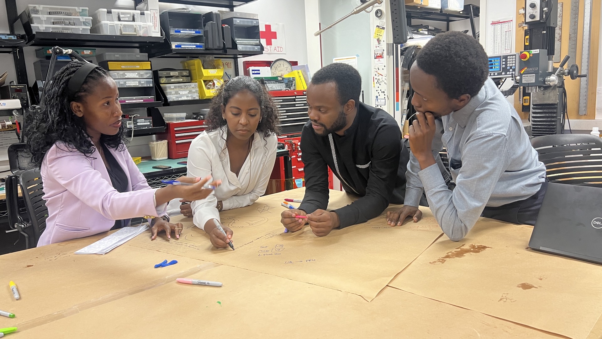 Four EAB fellows sketching concepts on butcher paper at a prototyping bench in the machine shop